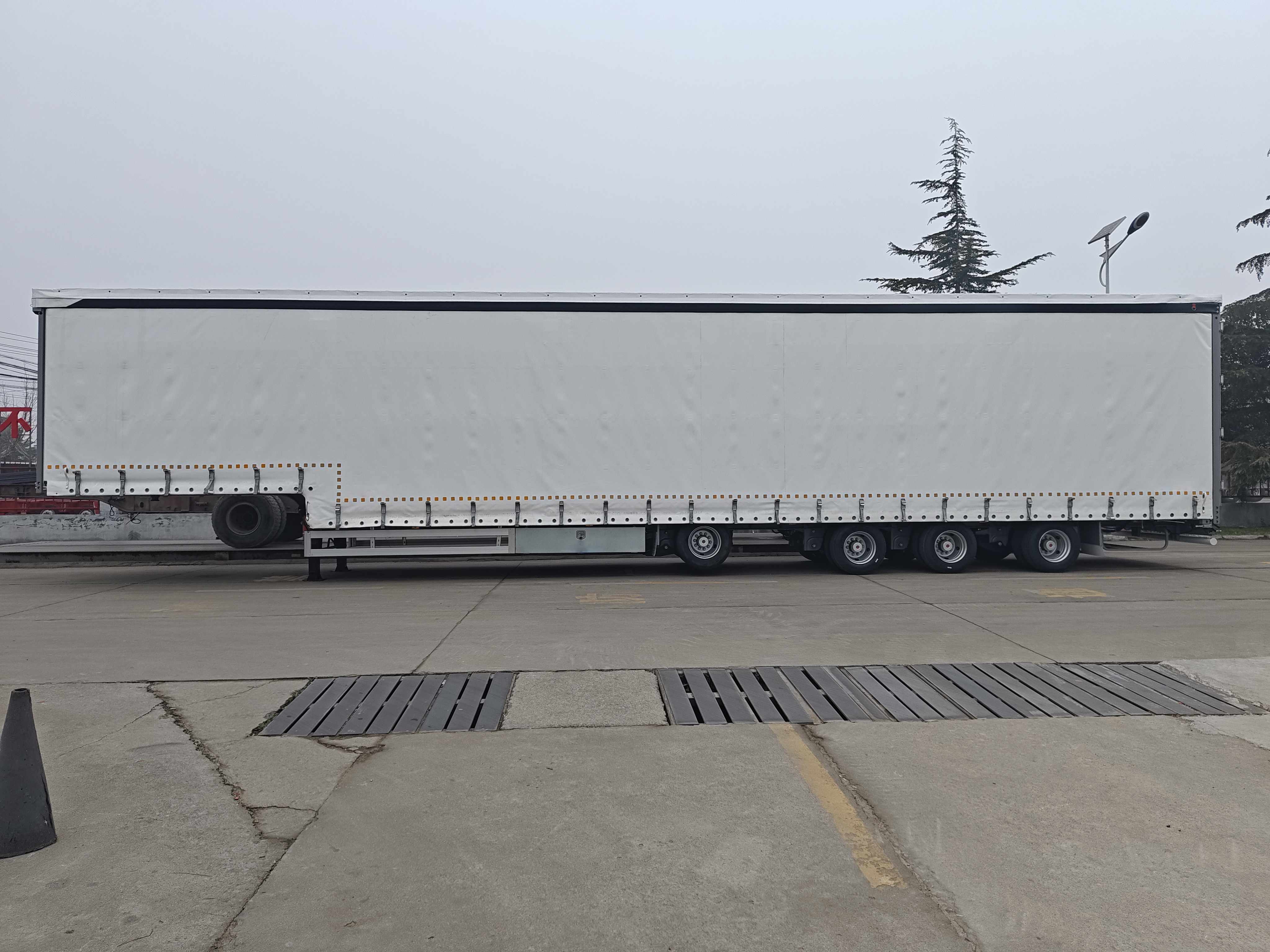 Full side profile of the tri-axle curtain side transport trailer showing the durable weather-resistant sliding curtains