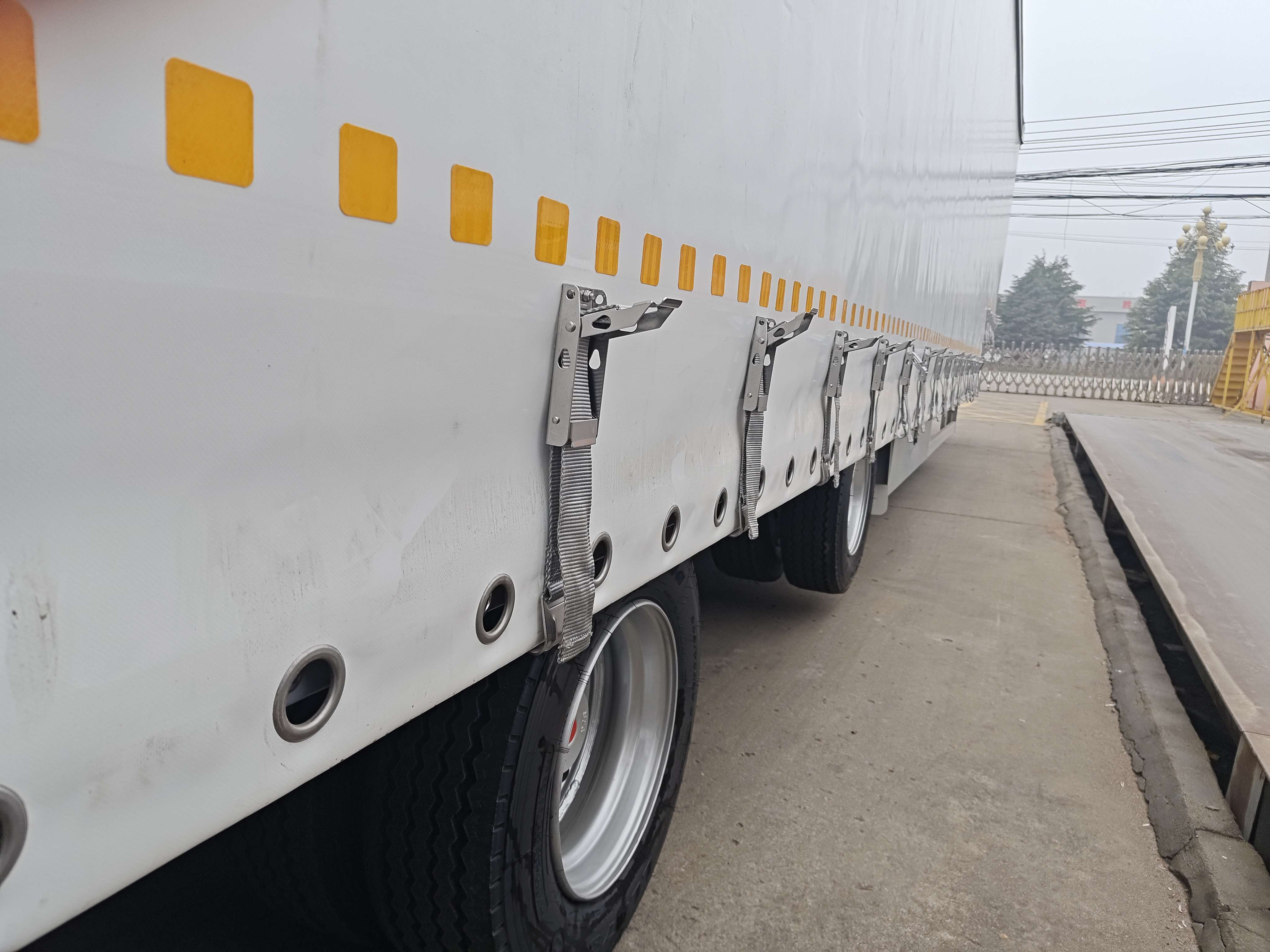 Detailed view of the stainless steel tension buckles and straps securing the heavy-duty PVC curtain on the semi-trailer