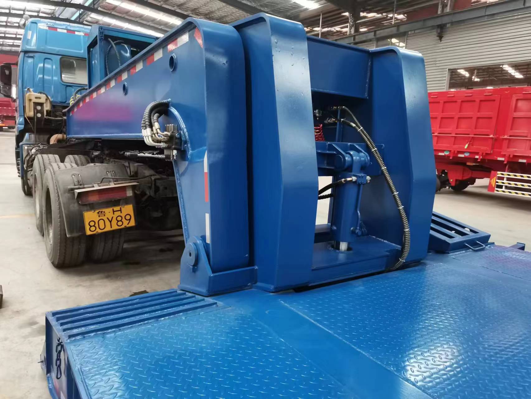 Detailed shot showcasing the heavy-duty side beams and extendable outriggers of the empty red RGN trailer's loading deck, providing flexibility for transporting oversized construction machinery