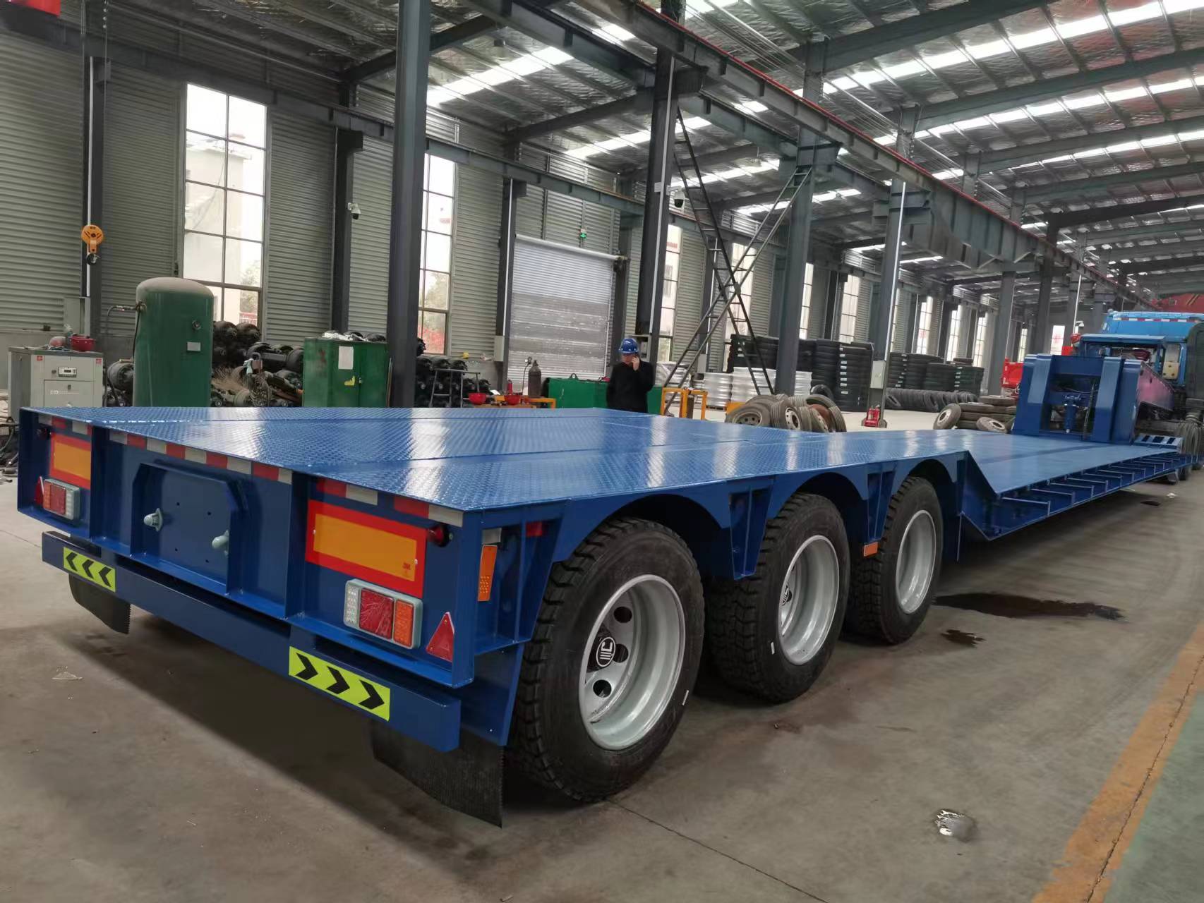 Technical close-up view focusing on the robust tandem axle suspension system of the empty red 3-axle removable gooseneck (RGN) lowboy trailer, engineered for heavy payloads on challenging Congolese terrain.