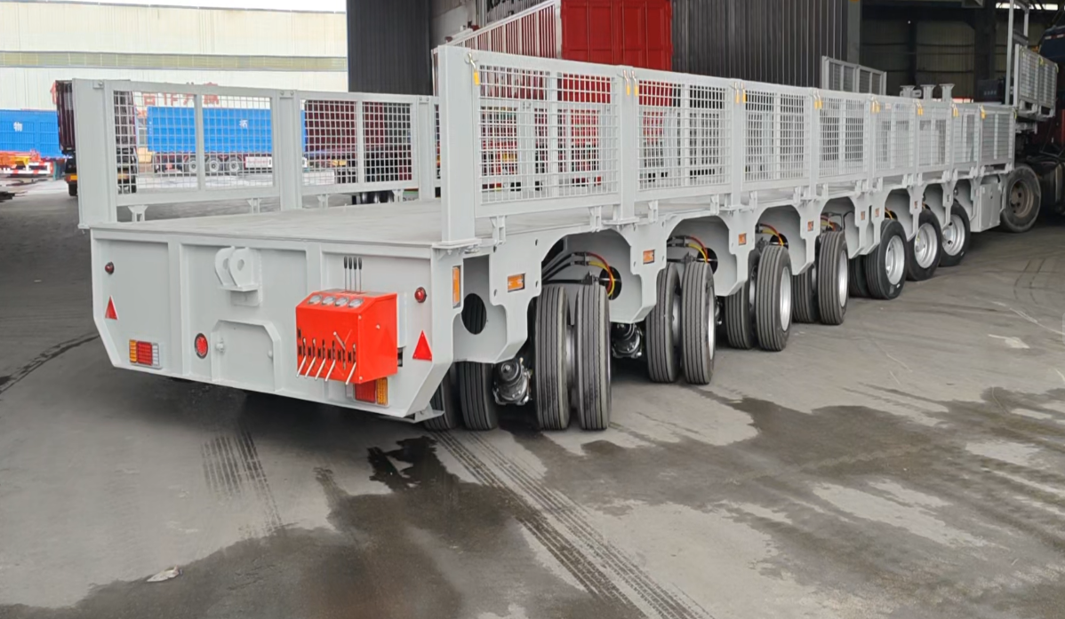 Lateral view of a HUAYUE multi-axle hydraulic trailer. The linkage steering system allows multiple rear wheel sets to adopt perfect steering angles, drastically reducing the turning radius.
