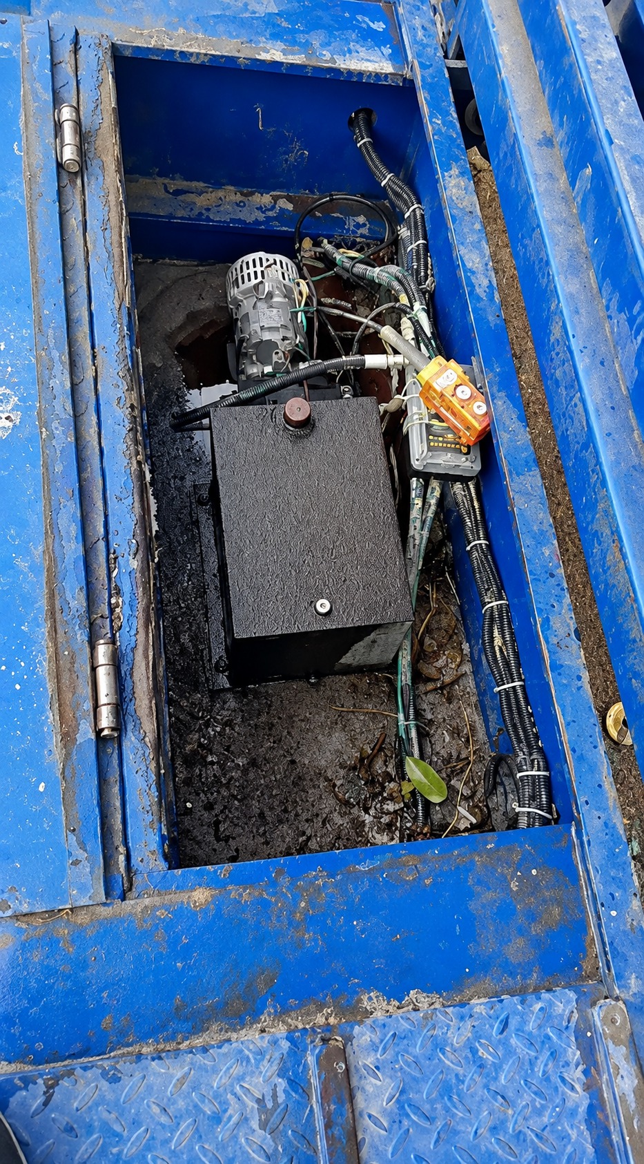 Hydraulic motor enclosure on an in-service blue trailer with standing water and debris visible