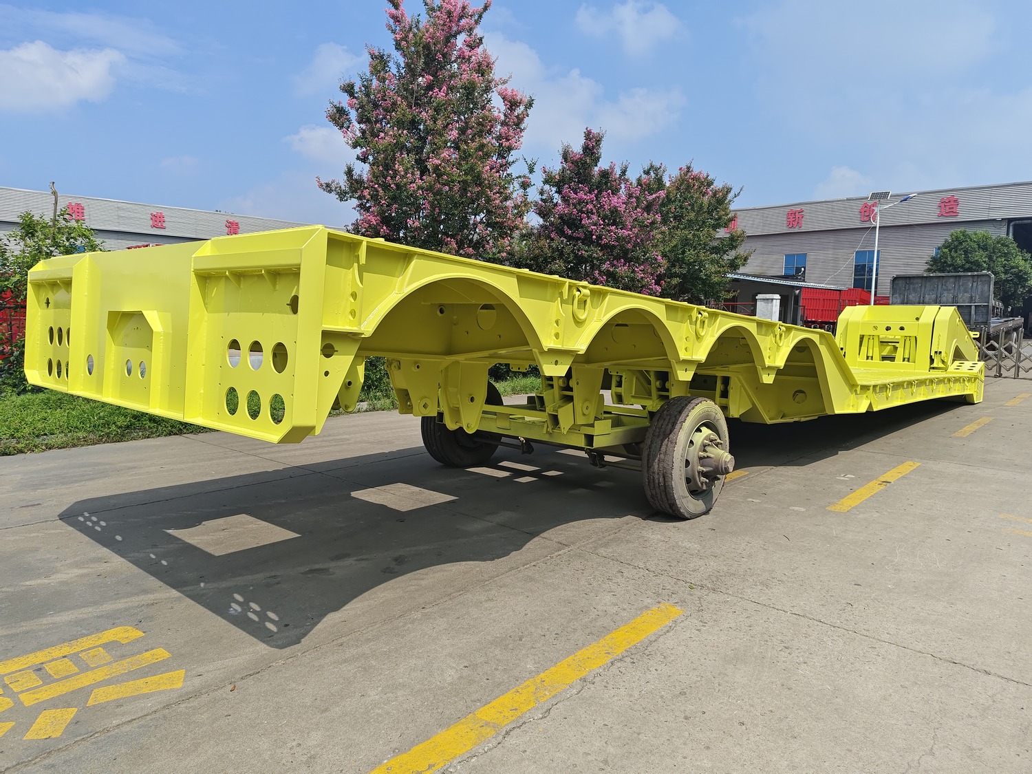 Yellow lowbed trailer chassis being prepared in a factory yard