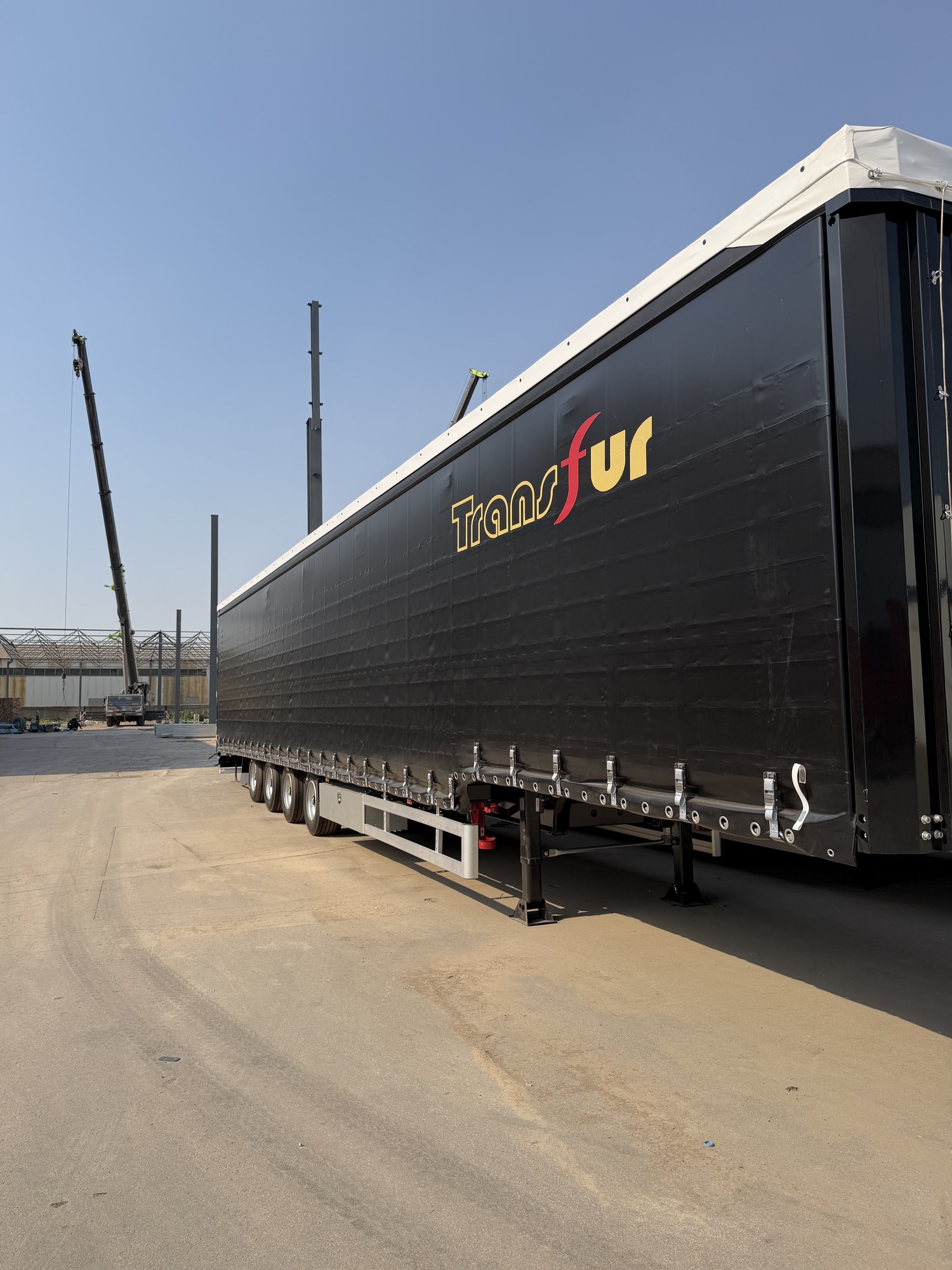 Electric curtain side trailer configuration Side view of a black curtain side semi-trailer in a factory yard