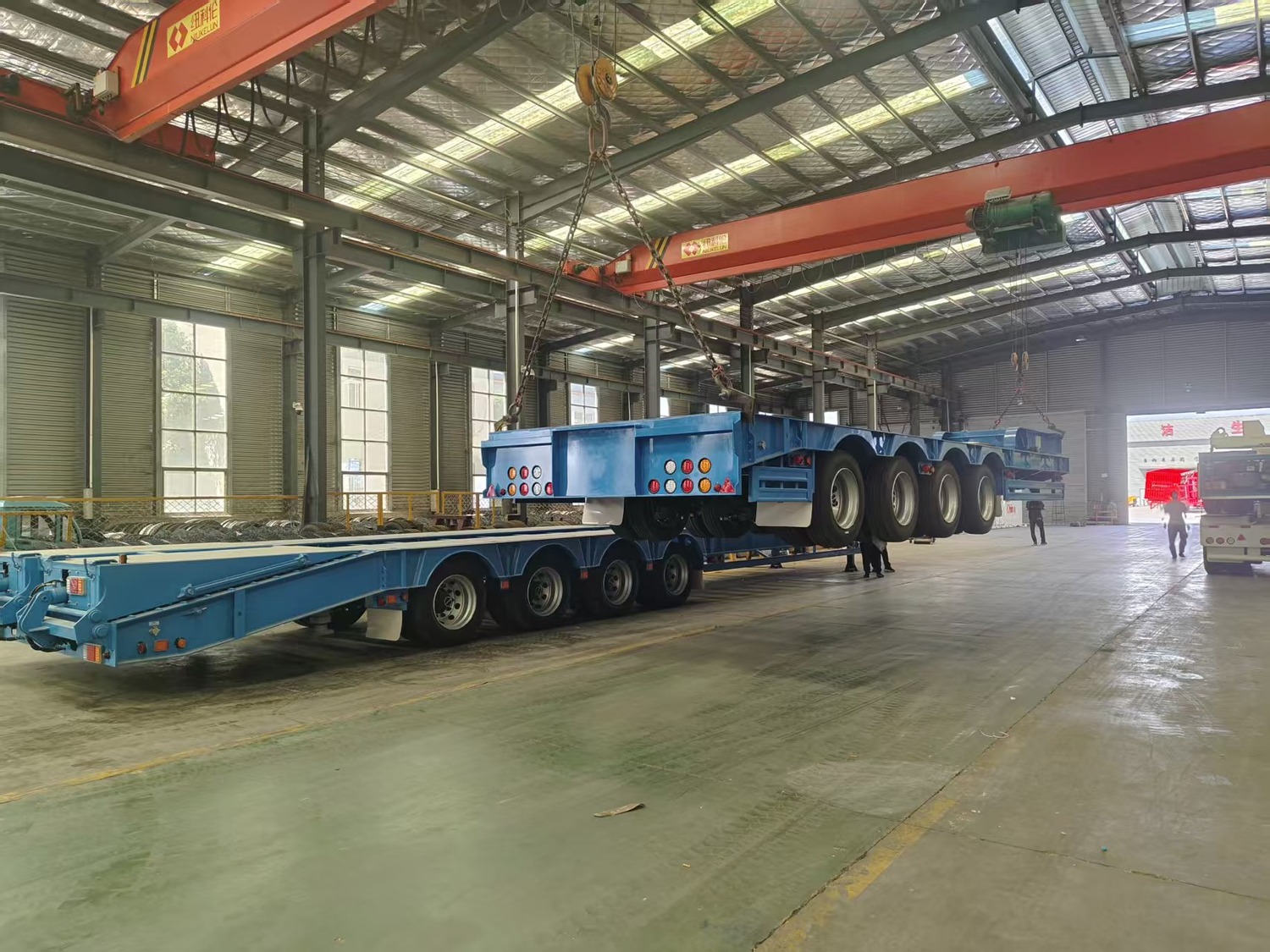 A 4-axle lowbed trailer being positioned by an overhead crane during workshop packing